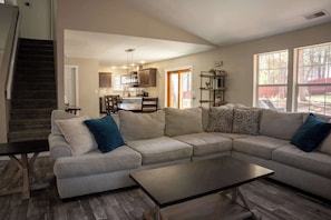 A living room with a sectional sofa, a coffee table, and a staircase.
