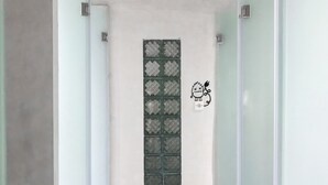 A hallway with a glass door featuring a geometric pattern, a wall-mounted light switch, and a cartoon character decoration. - Stellar Capsules - Hostel (Seminyak)
