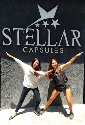 Two people posing in front of a wall with the text "STELLAR CAPSULES" and a star logo. - Stellar Capsules - Hostel (Seminyak)