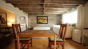 Une pièce chaleureuse avec une table à manger en bois, quatre chaises, un lit, une petite kitchenette et un tableau accroché au mur.