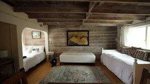 Une chambre avec deux lits, un banc, un tapis et un tableau au mur.