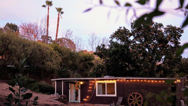 Une petite cabane avec une façade en bois, une roue et des guirlandes lumineuses.