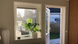 Ein Schlafzimmer mit einem Bett, einem Fenster mit Pflanze, einem Heizkörper und einer Tür, die nach draußen führt.