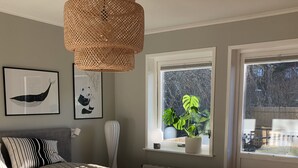 Ein Schlafzimmer mit einem großen Bett, einer hängenden Rattan-Lampe, einem Fenster mit Blick nach draußen und zwei gerahmten Tierabbildungen an der Wand.