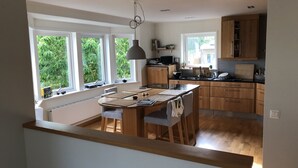 Eine moderne Küche mit Holzausstattung, ein Essbereich mit Tisch und Stühlen und große Fenster mit Blick auf Grünflächen.