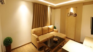 A modern living room with a beige sofa, a glass coffee table, and a small side table. - Hotel Radiance (Bareilly)