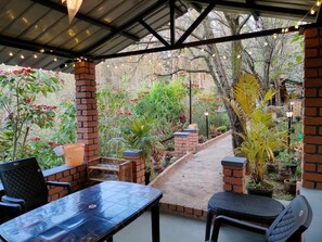 An outdoor patio with brick pillars, a table, chairs, and potted plants.