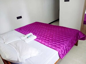 A single bed with a white mattress and pillows, a bright pink quilted bedspread, and a small bedside table with a lamp.