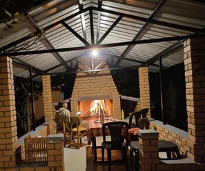An outdoor patio with a brick fireplace, seating, and a covered area with a metal roof.