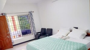 A bedroom with a bed, two chairs, a window with metal bars, and a door. - Pear Tree Inn (Kotagiri)