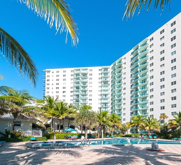 A high-rise hotel with multiple balconies, a swimming pool, and palm trees.