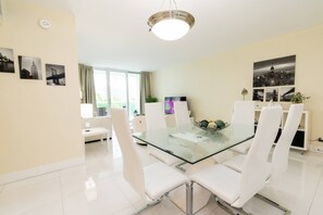 A modern dining area with a glass-top table, white chairs, and a cityscape view.