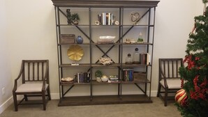 Ein Bücherregal aus Holz mit mehreren Ablagen, flankiert von zwei Holzstühlen, und ein Weihnachtsbaum mit roten Dekorationen.