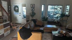 A spacious living room with a large sofa, a coffee table, and a rug. There is a staircase leading to another level, and a door with a window. - Luxury open concept Vacation Home. Close to downtown ,Old Mill trails & parks. (Bend)