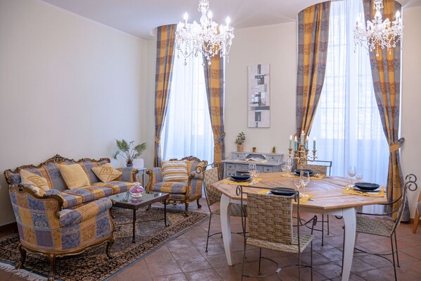 Ein Wohnzimmer mit einer Couch, einem Esstisch und Stühlen. Über dem Tisch hängt eine Pendelleuchte.