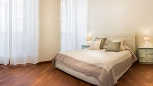 Ein ordentlich bezogenes Bett mit beige-farbener Bettdecke und Kissen, ein Holzboden und ein Nachttisch mit Lampe.