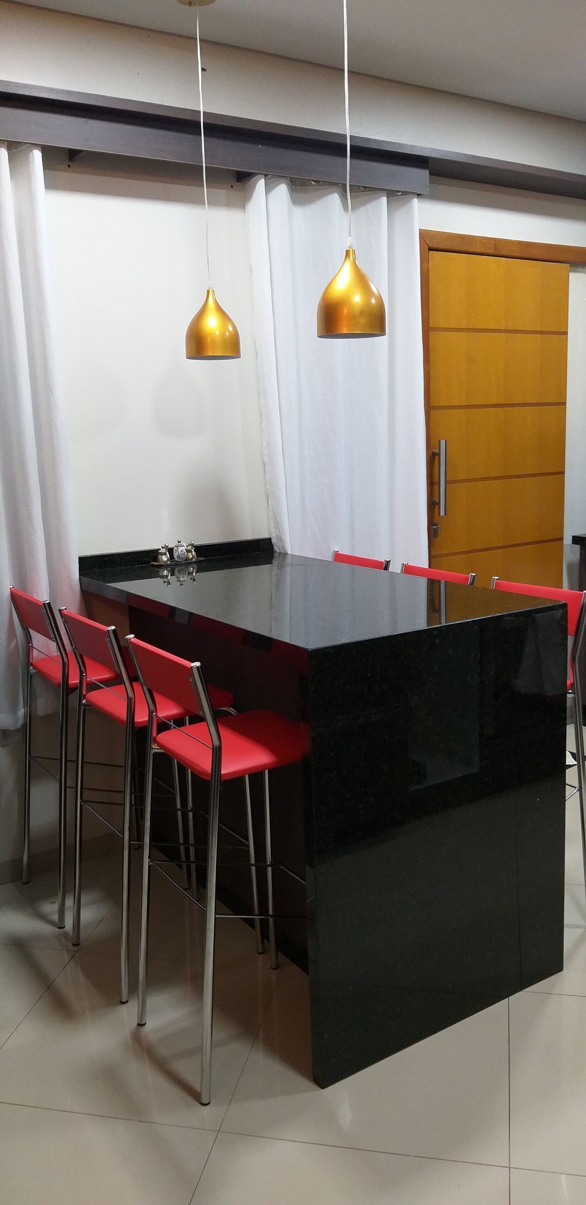 A modern dining area with a black island table, red chairs, and two gold pendant lights.