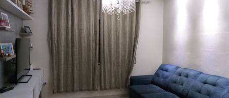 Un salón con un sofá azul, una araña y cortinas.
