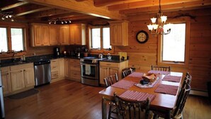 Cocina de cabaña de madera con armarios de madera, estufa, lavabo y una mesa de comedor con sillas.