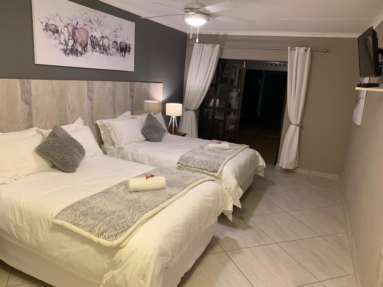 Une chambre d’hôtel avec deux lits, un ventilateur de plafond, un tableau au mur et une vue sur l’extérieur.