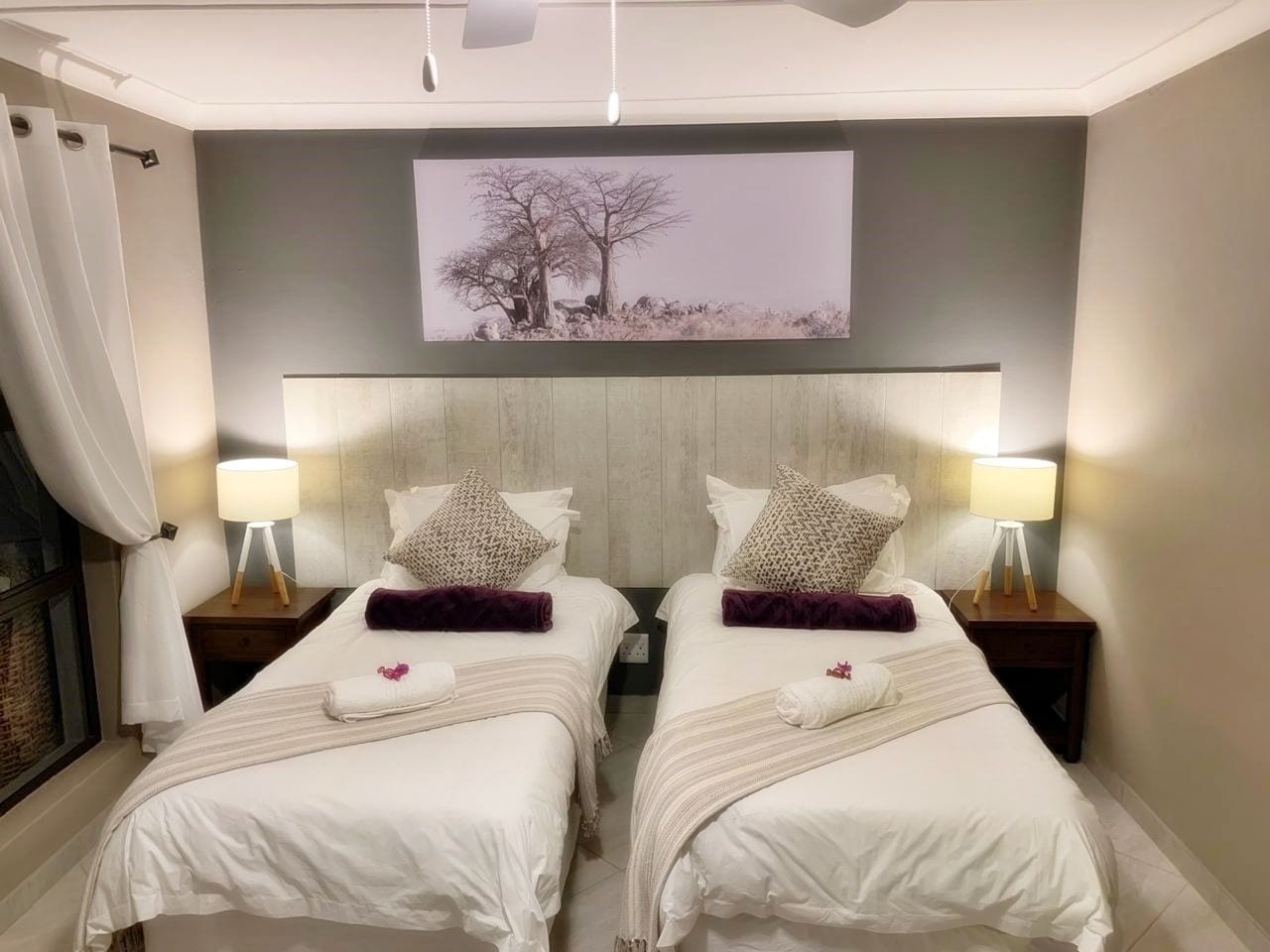 A hotel room with two beds, each with a pillow, a bedside lamp, and a framed picture on the wall.