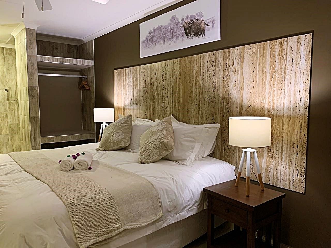 Una habitación de hotel con una cama grande, dos lámparas de noche, un cabecero de madera y un cuadro enmarcado en la pared.