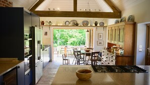 Une cuisine dotée d’un îlot central, un coin repas avec des sièges à l’extérieur, et une vue sur la verdure environnante.