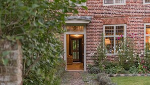 Un bâtiment en briques avec une entrée donnant sur un jardin, une porte bien visible et des fenêtres avec des rideaux.