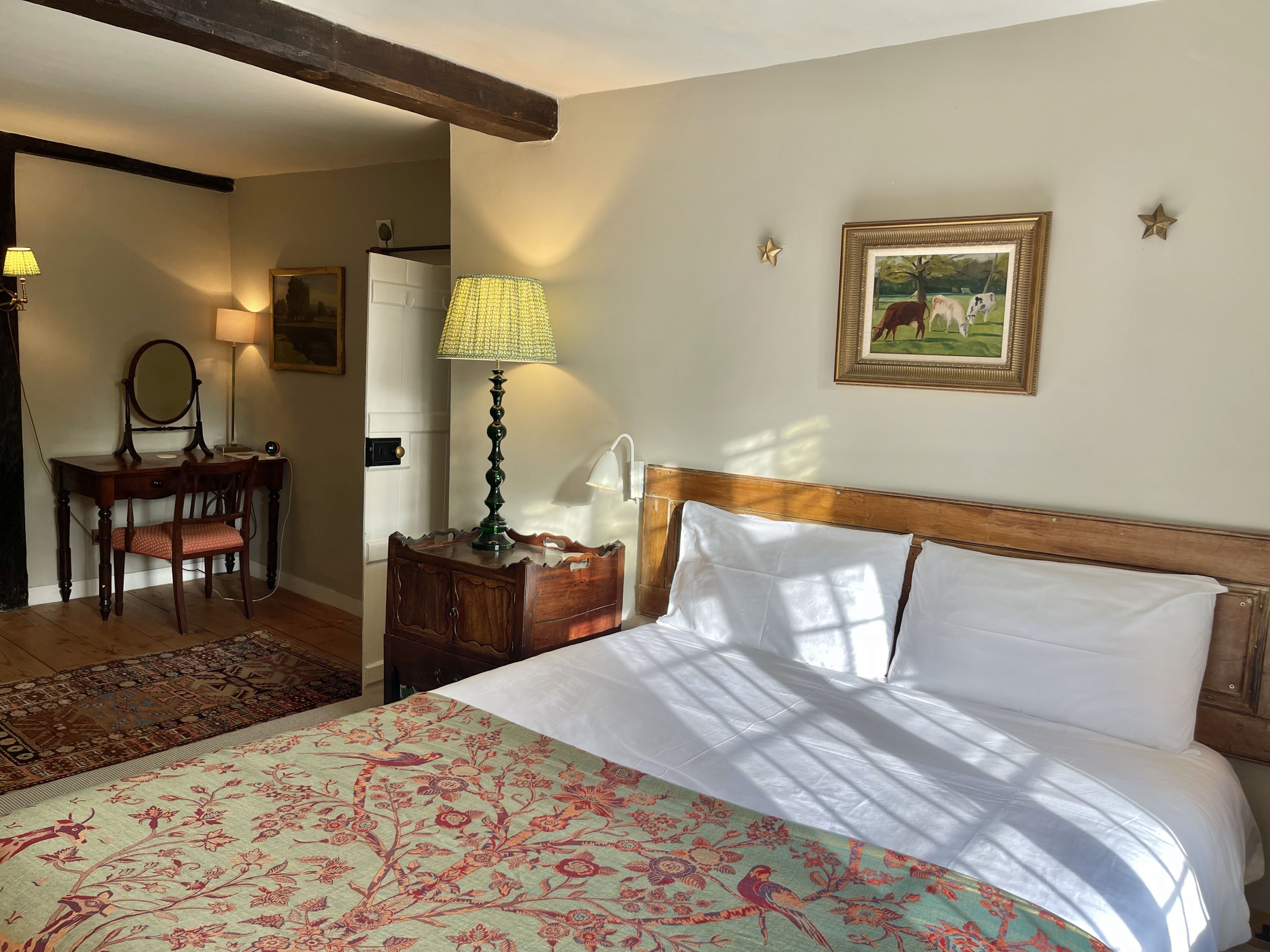 Une chambre à coucher avec un lit, un bureau avec une lampe, une chaise, une commode et un tableau accroché au mur.