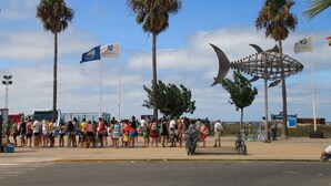 Una plaza pública con palmeras, una multitud de personas y una gran escultura de metal.