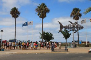 A public square with palm trees, a crowd of people, and a large metal sculpture. - Apartment with air-con in lounge (CONIL DE LA FRONTERA)