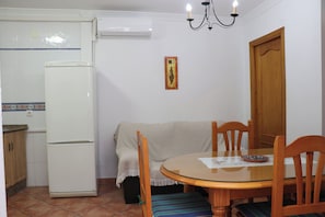 A compact kitchen with a refrigerator, a dining table with chairs, and a chandelier.