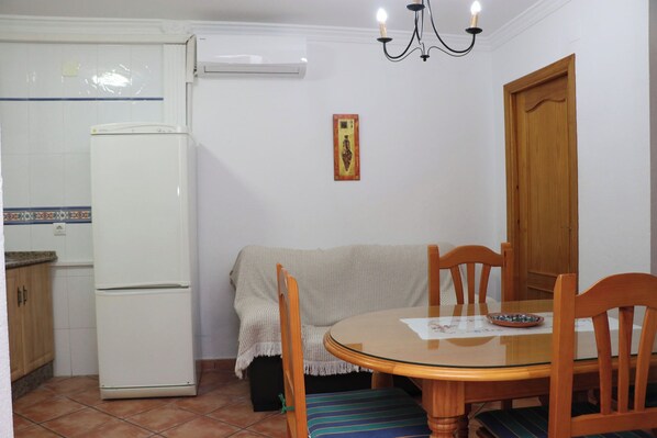 A compact kitchen with a refrigerator, a dining table with chairs, and a chandelier.