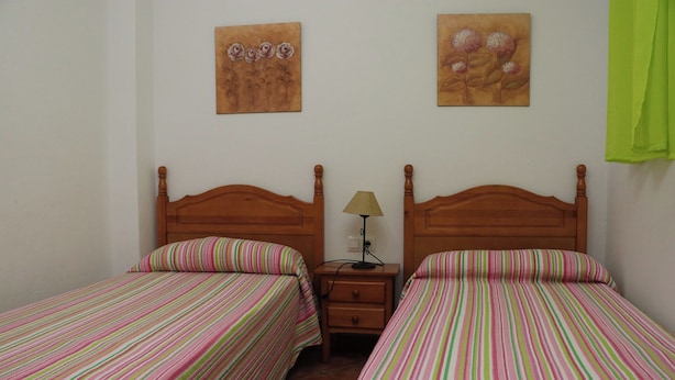 Una habitación con dos camas individuales, cabeceras de madera, ropa de cama a rayas, una mesita de noche con lámpara y dos cuadros colgados en la pared.