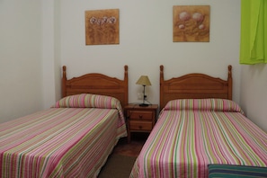 A room with two single beds, wooden headboards, striped bedding, a nightstand with a lamp, and two wall-mounted paintings. - Apartment with air-con in lounge (CONIL DE LA FRONTERA)