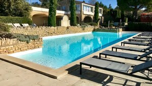 Una piscina con sillas de descanso, un muro de piedra y un edificio con arcos al fondo.