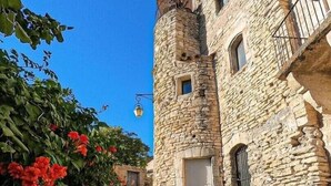 Un edificio de piedra con una torre, un sendero adoquinado y flores rojas.
