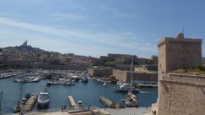 Un puerto con barcos amarrados, una fortaleza y un paisaje urbano al fondo.