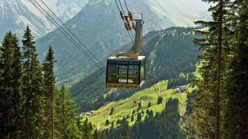 A cable car with 'brandneral' branding, suspended over a mountainous landscape with dense forests.