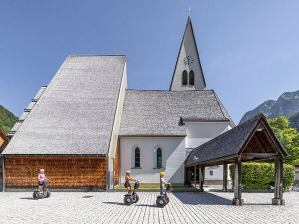 A church with a steeple, a wooden structure, and a paved area.