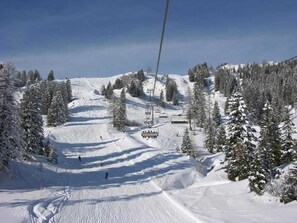 Pista de esquí nevada con telesilla y árboles.