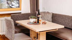 Un comedor con una mesa de madera, sillas acolchadas, una planta en maceta, una botella y un cuenco de fruta.