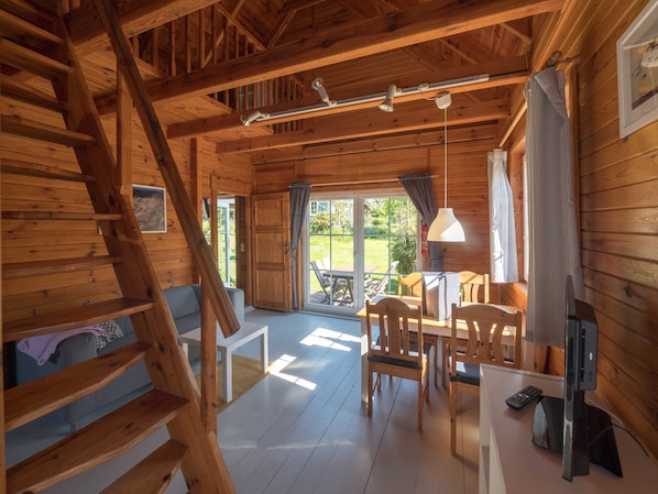 A wooden cabin interior with a dining area, a staircase, and a large sliding glass door leading to an outdoor patio.