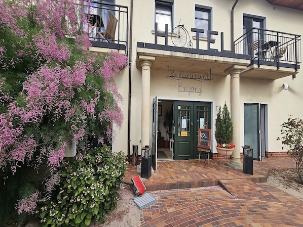 A restaurant with a balcony, a sign above the entrance, and a flower pot on the ground.