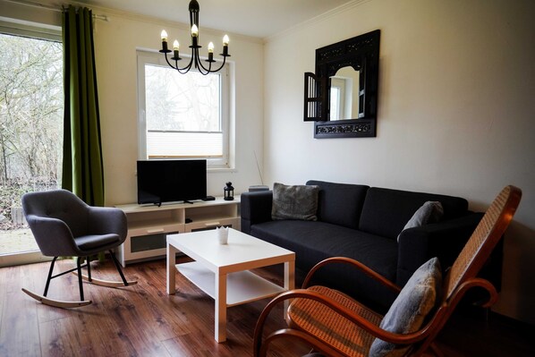 A living room with a black sofa, a white coffee table, a rocking chair, and a television on a stand.