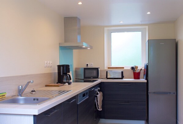 A compact kitchen with a sink, stove, microwave, toaster, and a refrigerator.
