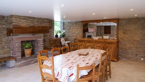 Un coin repas agrémenté d’une cheminée en pierre, de chaises en bois, d’une table recouverte d’une nappe rouge et blanche, et d’un mur en pierre.