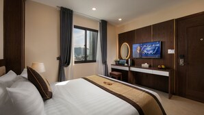 A hotel room with a large bed, a desk with a TV, a mirror, and a view of the city through the window.