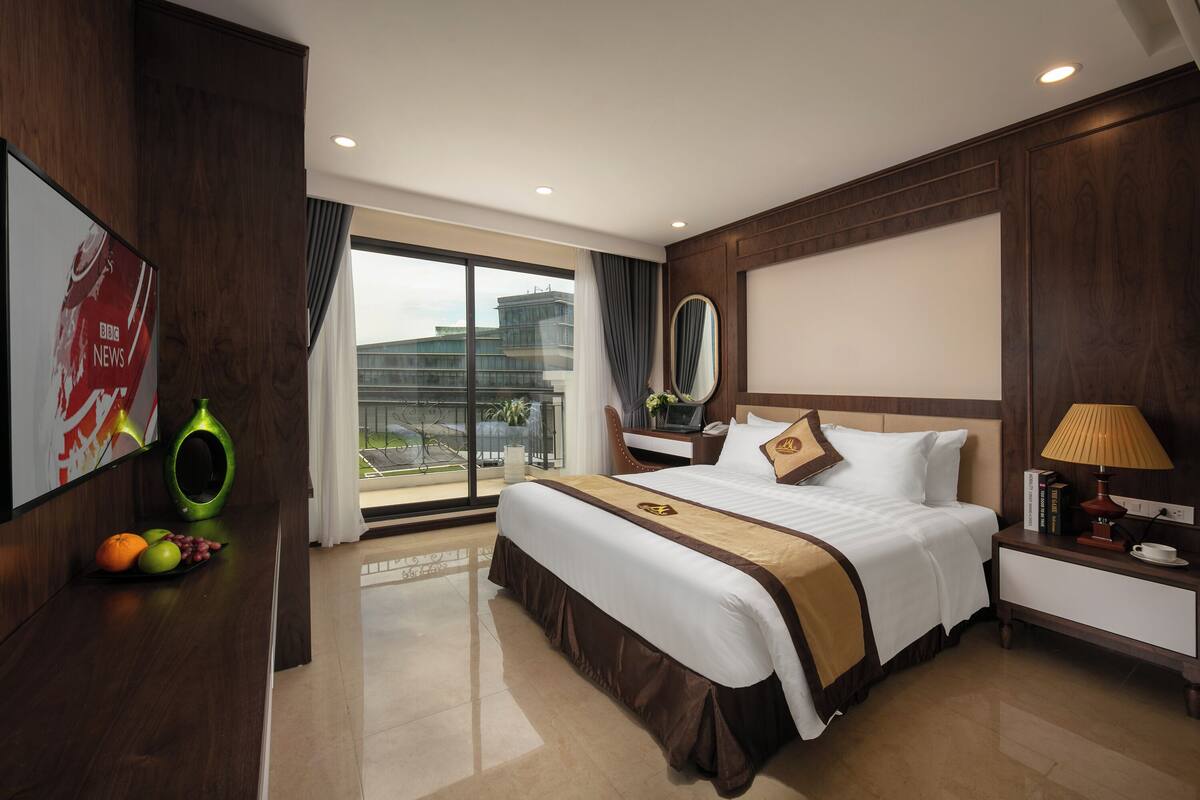 A hotel room with a large bed, a desk, a chair, a TV, and a view of the city.