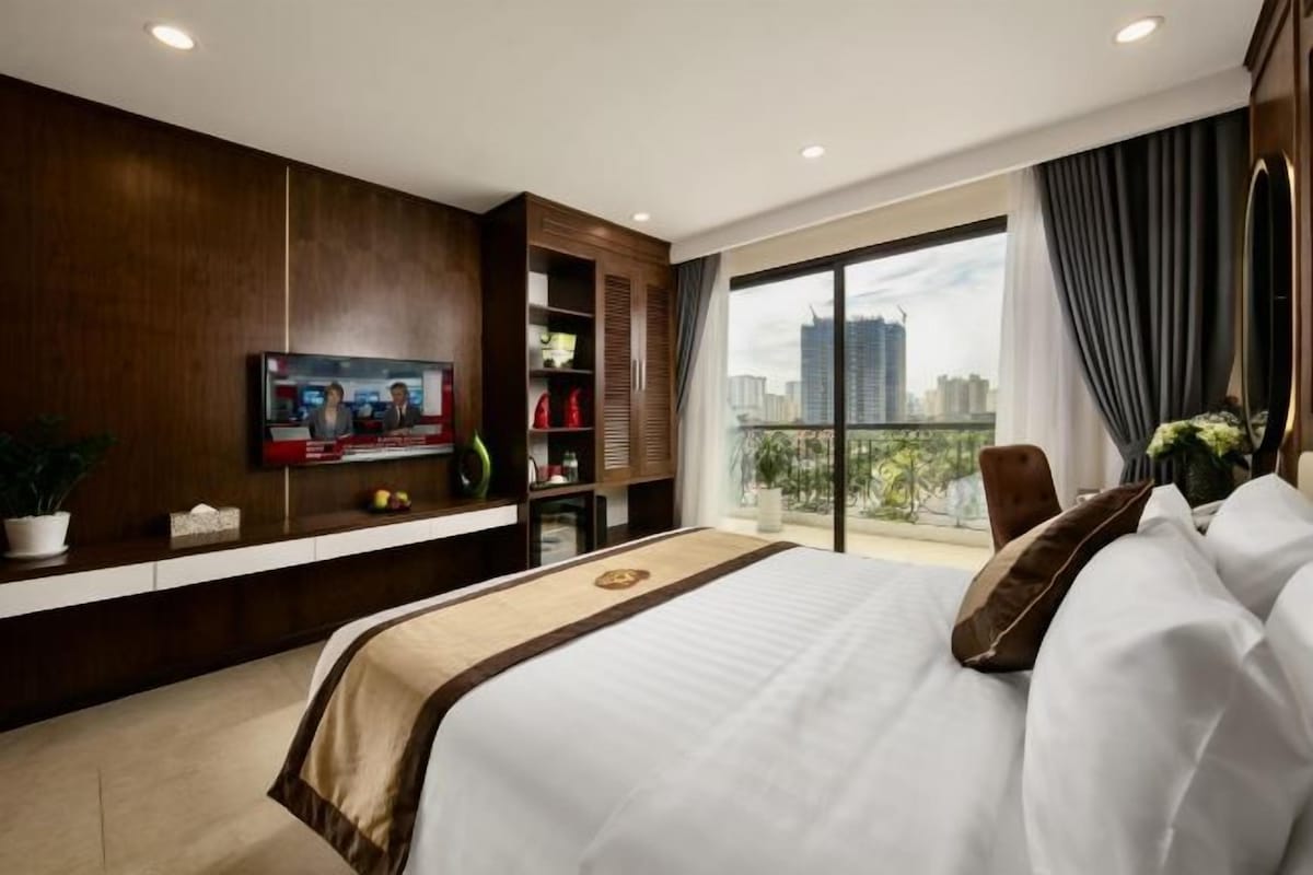 Een moderne hotelkamer met een groot bed, een aan de muur bevestigde televisie, een balkon met uitzicht op de stad en een houten garderobekast.